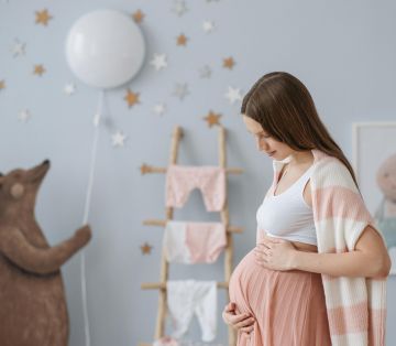 Schwangere Frau in Kinderzimmer, fürsorglich ihren Bauch haltend